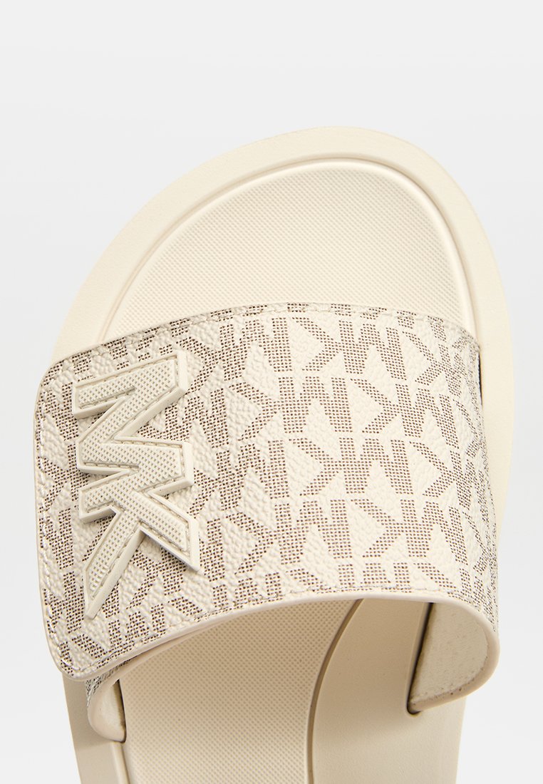 Beige Riemchensandale mit einem Musterstoffriemen, der ein erhabenes Logo aufweist. Die Sohle ist glatt und strukturiert für besseren Halt.
