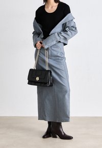 Falda maxi de denim con costuras laterales, blusa negra de manga corta, chaqueta gris corta, bolso acolchado negro y botas de tacón marrones.