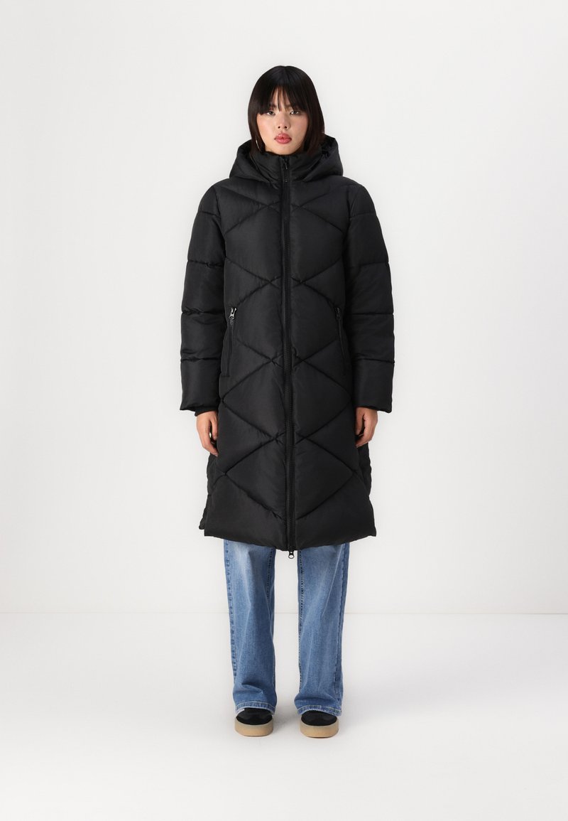 Long black puffer coat with a diamond quilted pattern, hood, and zipper pockets, paired with blue jeans and black shoes.