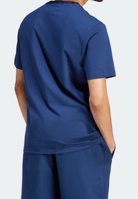 Námořnická modrá bavlněná trička s krátkým rukávem a kulatým výstřihem. Hladká textura, volný střih a viditelné švy podél ramen.