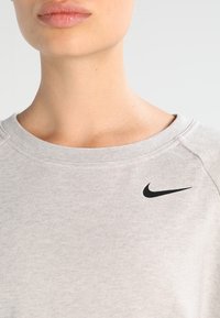 Sweatshirt gris clair en tissu doux, avec un col rond et un logo Nike noir sur la poitrine, présentant une texture côtelée et des détails de couture.