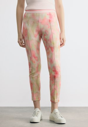 Γυναίκα που φοράει παντελόνια στενής γραμμής μέχρι τον αστράγαλο με ροζ και μπεζ αφηρημένο μοτίβο, συνδυασμένα με λευκά αθλητικά παπούτσια.