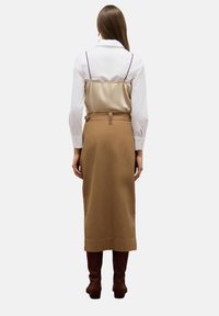 Bruine midi-rok, beige satijnen top met dunne zwarte bandjes, witte blouse, en bruine kniehoge laarzen, gezien vanuit de achterkant.