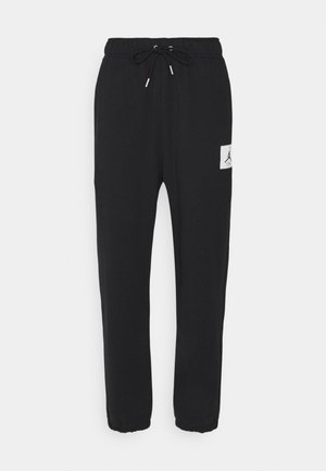 Schwarze Sweatpants mit elastischem Bund und Kordelzug, zulaufende Beine mit Bündchen und einem weißen, rechteckigen Logo-Patch am rechten Oberschenkel.
