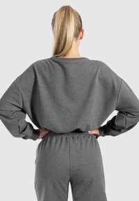 Felpa grigia con vestibilità ampia e spalle scese, abbinata a pantaloni jogger grigi coordinati. Tessuto liscio, cintura elastica, design minimale.