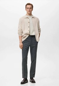 Jasnobeżowy kardigan z guzikami, biały sweter i dopasowane ciemnoszare spodnie. Strój wyróżnia się gładką fakturą i klasycznym wzornictwem.