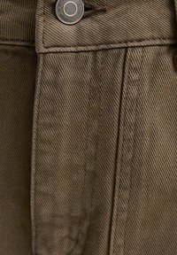 Close-up van olijfgroen stof met diagonale weving, verticale naad en metalen knoopsluiting aan de tailleband.