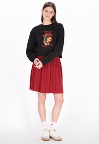 Sudadera negra con gráfico de oso colorido, combinada con una falda plisada roja. Calcetines blancos con corazones rojos y zapatillas blancas completan el conjunto.