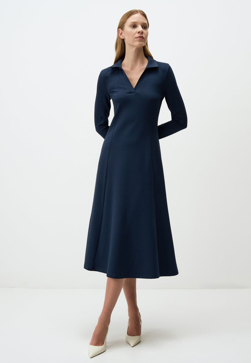 Robe navy à manches longues avec col, corsage structuré, jupe évasée et texture lisse. Présente un décolleté en V et une longueur mi-mollet.