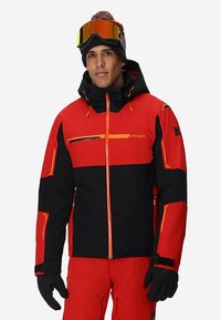 Rode en zwarte ski-jas met capuchon, voorzien van oranje accenten, ritsen, zakdetail en verstelbare manchetten. Ideaal voor wintersport.