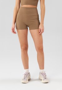 Ensemble de sport marron côtelé comprenant un haut court et un short taille haute, assorti à des chaussures de sport de couleur claire et des chaussettes blanches.