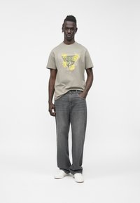 Gaiši pelēka T-krekls ar dzeltens ziedu grafiku, kombinēts ar tumši pelēnām plata piegriezuma džinsiem un baltiem sporta apaviem. Vienkāršs apaļš kakla izgriezums.