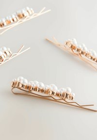 Roségoldene Haarnadeln mit weißen Kunstperlen, die in einer Gruppe entlang der oberen Kante angeordnet sind; strukturierte und glatte Oberflächen verbessern das Design.