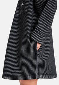 Schwarz-weiß gestreiftes Kleid mit lässiger Passform, featuring einer Brusttasche und umgeschlagenen Ärmeln, gefertigt aus einem weichen Stoff.