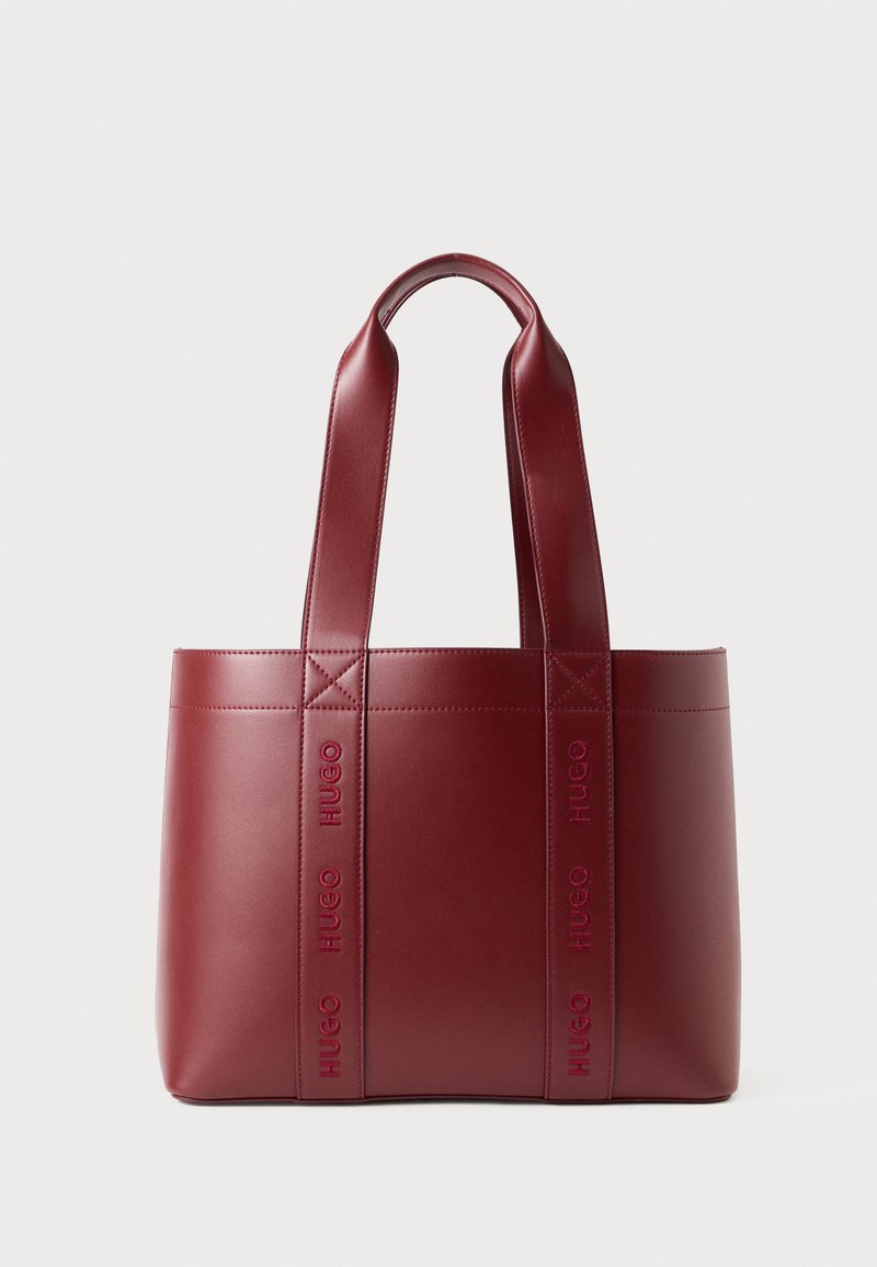 Borsa tote in pelle rossa scura con manici larghi, caratterizzata da un motivo in rilievo ripetuto con il branding "HUGO" sulle cinghie, su uno sfondo semplice e chiaro.