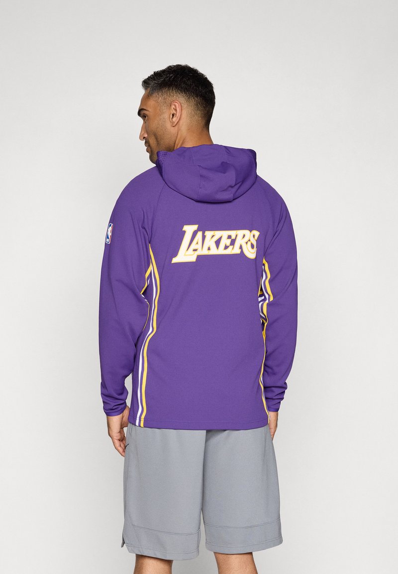 Lila Kapuzenpullover mit "LAKERS" in Gelb auf dem Rücken, gelben Seitenakzenten und NBA-Logo auf dem Ärmel.