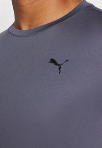 Grå treningsgenser med rund hals og glatt tekstur, med en svart Puma-logo på brystområdet.