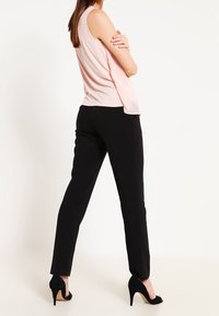 Top sin mangas de color rosa claro combinado con pantalones negros ajustados y tacones altos negros; tejido suave y diseño a medida.