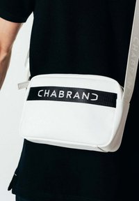 Borsa a tracolla bianca con una texture liscia, dotata di una tracolla in tessuto nera con la scritta "CHABRAND" stampata in bianco. Include una tracolla regolabile.