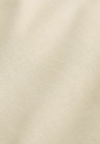 Tissu beige avec une texture fine et lisse et un motif côtelé subtil, éclairé doucement pour mettre en valeur les plis délicats et les détails du tissage.