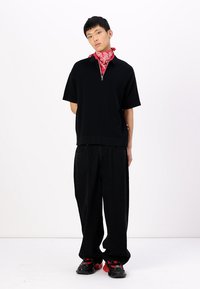 Black short-sleeve zippered top, loose black pants, red bandana around the neck, and black shoes with red accents. Minimalist design.
