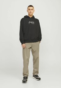 Sudadera negra de algodón con bolsillo tipo canguro y texto blanco en el logo, combinada con pantalones chinos color beige y zapatillas negras con parte superior de malla y suela de goma.
