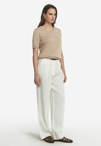 Beige V-hals t-shirt med korte ærmer, hvide bukser med vidde og brune sandalromper, præsenterer glatte teksturer og en afslappet pasform.