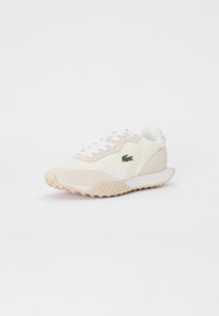 Baskets Lacoste en crème et beige, associant un mélange de daim et de matériaux synthétiques, semelle texturée et logo sur le côté.