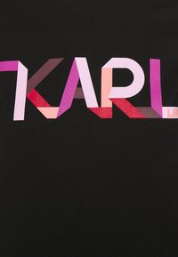 Camiseta negra con un atrevido gráfico "KARL" en colores vibrantes, con formas geométricas en tonos de rosa, púrpura y rojo en la zona del pecho.