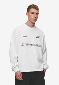 White long-sleeve sweatshirt featuring a graphic print with 'P' and 'POWER' in black and red accents. Soft cotton fabric, relaxed fit.