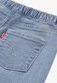 Ανοιχτό μπλε τζιν παντελόνι με ελαστική μέση, με πίσω τσέπη που έχει σχέδιο καρδιάς με ραφή και κόκκινη ετικέτα μάρκας.