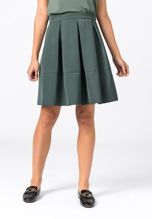 Une jupe plissée verte, arrivant au genou, fabriquée en tissu lisse et léger, avec une taille ajustée et un design épuré et structuré.