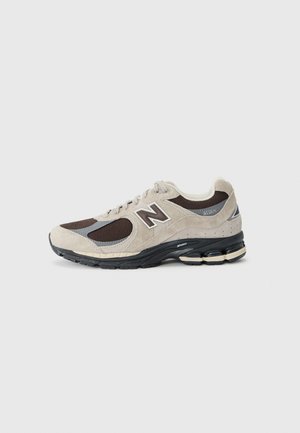 Scarpa New Balance 2002R beige e marrone con suola nera, pannelli in mesh e pelle scamosciata, e un sistema di ammortizzazione visibile nel tallone.