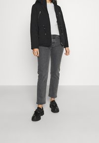 Svart vadderad jacka med huva, grå ribbad tröja, grå raka jeans och svarta plattformsskor med snörning.