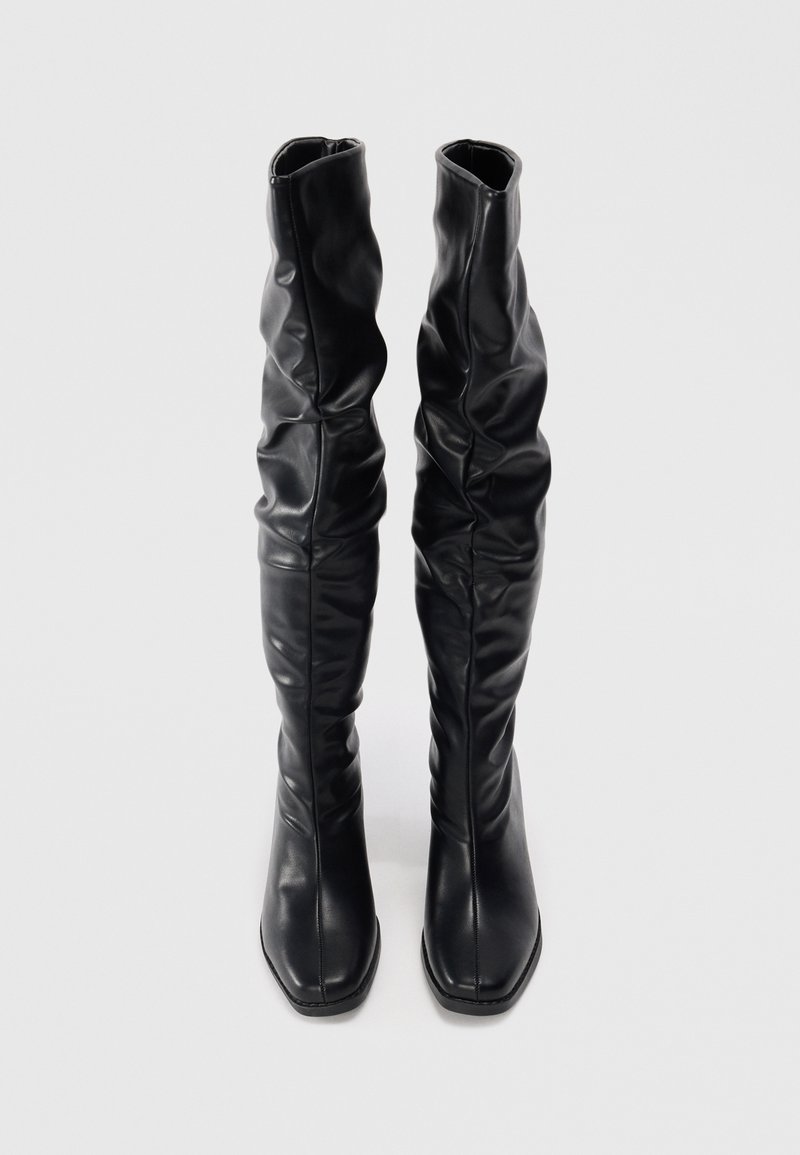 Bottes noires en cuir montantes avec un design décontracté, bout carré, texture lisse et détails de couture le long de la tige.