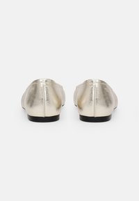 Metalliske gull ballet flats med en glatt tekstur, rund tå og svarte flate såler. Enkel design, ingen synlig maskinvare eller aksenter.