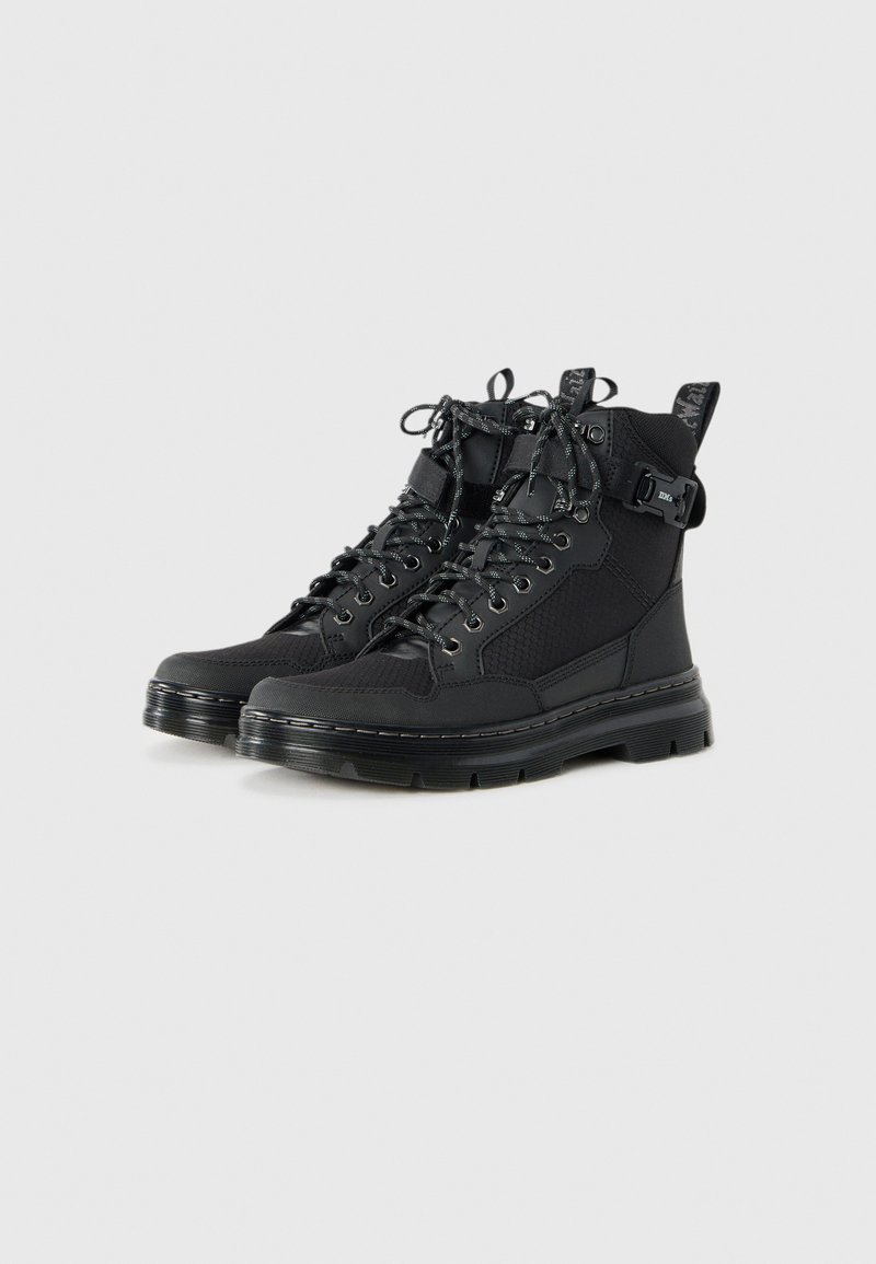 Bottes montantes noires avec des panneaux texturés, des lacets sur le devant, des sangles à boucle, des semelles épaisses et des languettes d'enfilage sur un fond blanc.