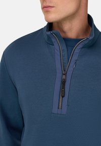 Sudadera de forro polar en azul oscuro con cuello alto, diseño con media cremallera y detalles en azul marino contrastantes. Presenta una textura suave y cremallera con marca.