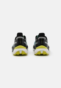 Scarpe da ginnastica nere con tomaia strutturata, dettagli verdi e intersuola bianca. La suola presenta un motivo in gomma gialla antiscivolo.