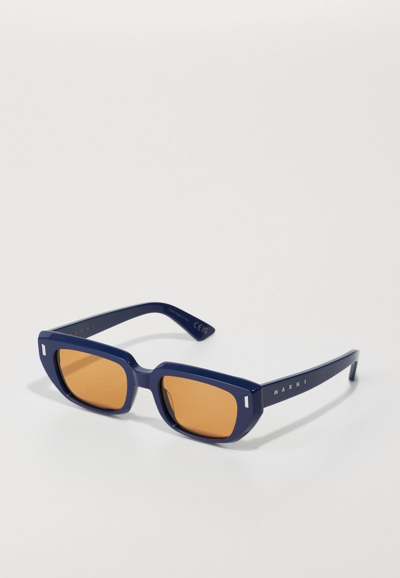 Tumesinine ristkülikukujuline päikeseprillid, millel on merevaiguvärvi objektiivid, paks plastikraam ja peen bränding templitel. Omab ruudukujulist objektiivi kuju.