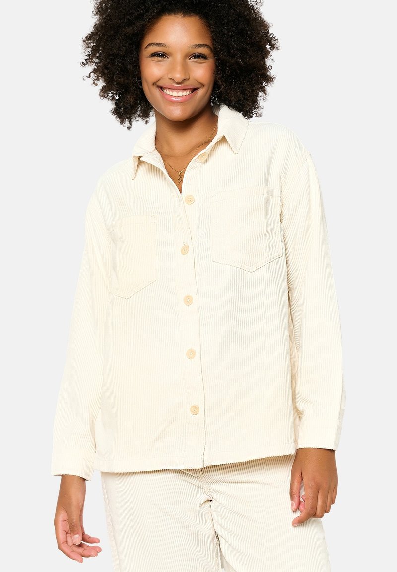 Cream corduroy button-up shirt with two chest pockets, long sleeves, and a collar. The texture is ribbed, creating a soft, cozy appearance.