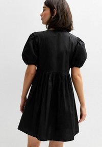 Vestido negro de mangas abullonadas con un corsé ajustado, cintura fruncida y falda acampanada. Hecho de una tela suave con un ligero brillo.