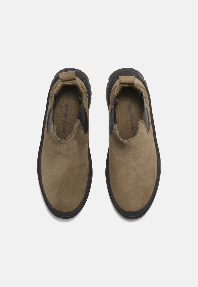 Bruine suède instappers met zwarte elastische zijaccenten en een rubberen zool. Kenmerkend zijn de soepele textuur en het ronde puntontwerp.