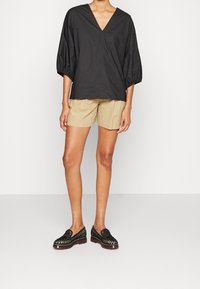Blusa nera, oversize, con scollatura a V e maniche a sbuffo, abbinata a pantaloni beige. Scarpe nere con texture a motivo e suola spessa.