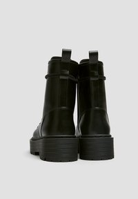 Bottes courtes en cuir noir avec une semelle épaisse, dotées d'une texture lisse, d'une languette de tirage et de coutures minimales à l'arrière.