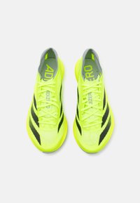 Neonsyellow sportske cipele s crnim prugama, lagani mrežasti gornji dio, ravne vezice i podstavljeni đon; istaknuti brend na jeziku.