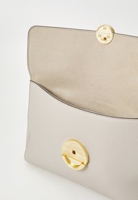 Porte-monnaie en cuir gris clair avec une texture lisse, doté d'un fermoir rond doré et d'une doublure intérieure beige douce.