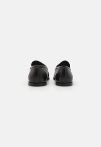 Melnas ādas loafers ar noapaļotu purngalu, šauru profilu un minimālām šuvēm, uz plakana gumijas pamatnes.