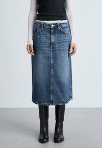 Blauwe denim rok tot de knie met een rechte snit, voorzien van een voornaad en klassieke vijfzakkenstijl, gedragen met hoge bruine laarzen.