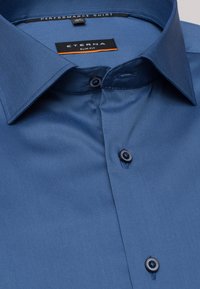 Slim fit performance shirt in een solide blauwe stof, met een gestructureerde kraag, knoopsluiting aan de voorkant en donkere knopen, met een soepele, subtiele textuur.